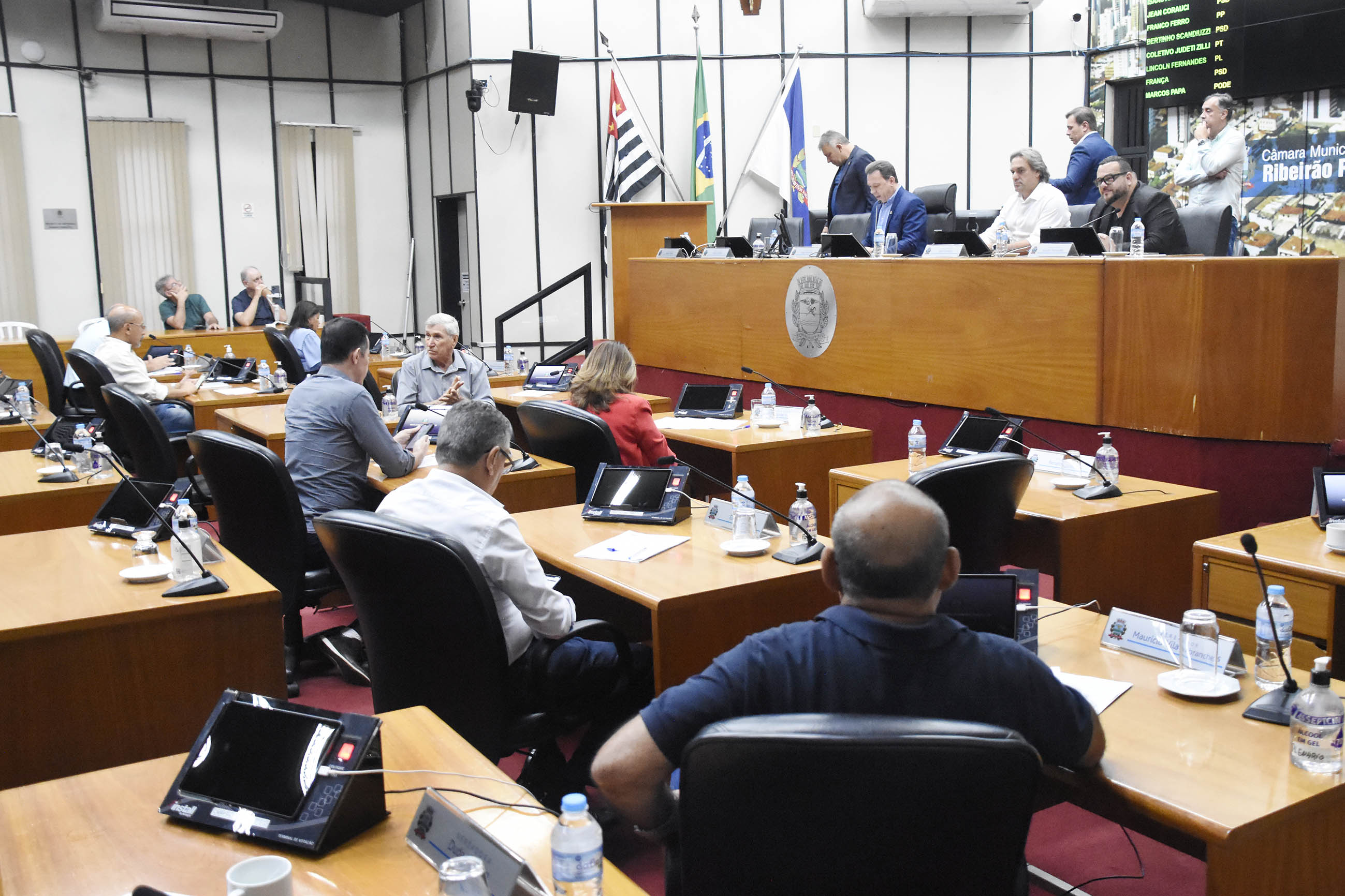 Imagem aberta do Plenário com a Mesa Diretora de frente e outros vereadores de costas